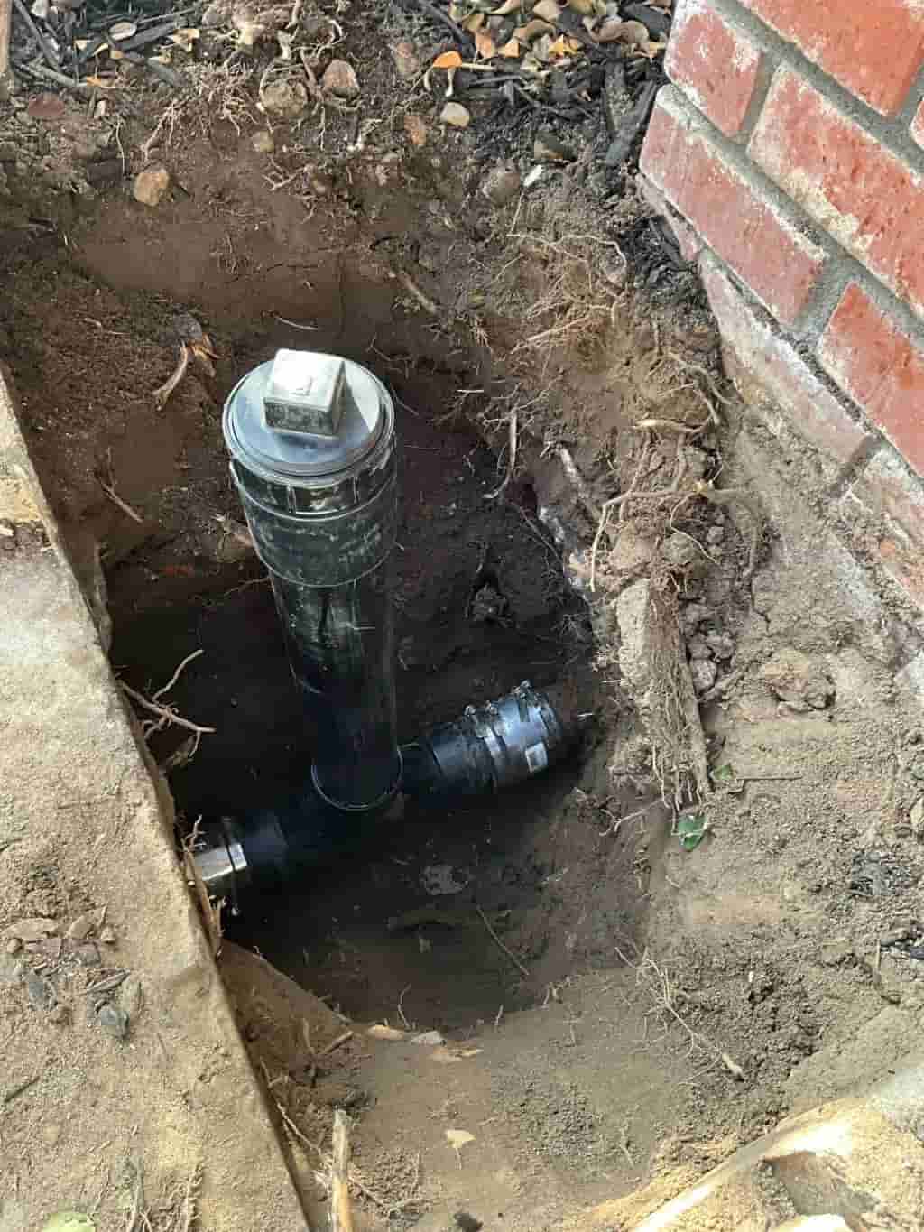 Plumber installing a black ABS sewer cleanout pipe with square cap for underground leak detection and main line inspection