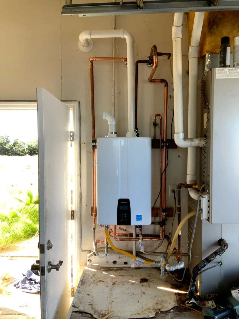 A professionally installed Navien tankless water heater system with extensive copper plumbing and PVC venting in a residential garage.